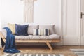 Blue blanket and cushions on beige wooden sofa in white loft interior with door. Real photo