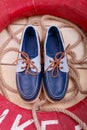Blue boat shoes on wooden background near red lifebuoy and rope. Top view. Royalty Free Stock Photo