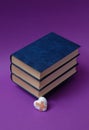 Blue books, hardcover, stacked horizontally, one on top of the other, a broken little white heart with patches, on a purple Royalty Free Stock Photo