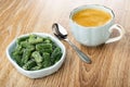 Bowl with marmalade in form green bean, spoon, coffee in cup on wooden table Royalty Free Stock Photo