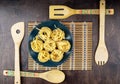 A blue bowl of fettuccine paste on a bamboo napkin and wooden spatulas on a mahogany background