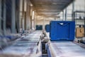 Blue boxes in a large, fully automated logistics warehouse run on a conveyor belt. Background is blurred. It is a modern storage