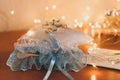 Blue bride garter with ribbon near decorative cushion with golden wedding rings in front of blurred shiny backdrop