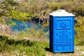 Blue Cabine Of Chemical Toilet In a Mountain Park on river background at sunny Summer Day