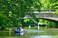 Blue canoe with a young family in front of a bridge over a small river in the big city with red paddles under the trees Royalty Free Stock Photo
