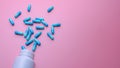 Blue capsule pills spread out of white plastic drug bottle on pink background. Pharmacy banner. Online pharmacy. Painkiller