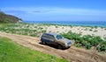 Blue car covered in mud on dirt road to a beach Royalty Free Stock Photo