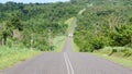 Blue car driving down empty asphalt road running past dense tropical vegetation Royalty Free Stock Photo