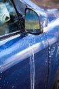 Blue car side mirror and door with foam during car washing, close-up view Royalty Free Stock Photo