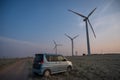 Blue car at windmills at sunset. Alternative energy source.