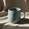 A blue ceramic mug with a speckled texture sits on a light beige, textured fabric. The Royalty Free Stock Photo