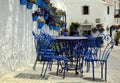 Blue chairs and tables, next to traditional blue plant pots with Geraniums, attached to a white-washed wall, Spain Royalty Free Stock Photo