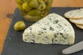 Blue cheese wedge with defocused jar of green olives and cracker