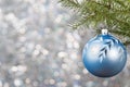 Blue Christmas ball on a Christmas tree branch over blurred shiny background, close up.