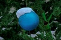 A blue Christmas ball hangs on a snow-covered branch of a Christmas tree on a festive background of white snow and snowy bokeh Royalty Free Stock Photo