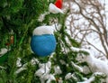 A blue Christmas ball hangs on a snow-covered branch of a Christmas tree on a festive background of white snow and snowy bokeh Royalty Free Stock Photo