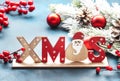 Blue Christmas or New Year background with red Christmas balls, berries, fir branches, pine cones and inscription Xmas