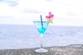 Blue cocktail in a martini glass with pink flower garnish and st Royalty Free Stock Photo