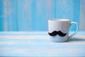 Blue coffee cup with Black mustache on wood table background in the morning. Father, International men day, Prostate Cancer
