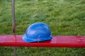 Blue color construction helmet on a red plastic bench. Green grass in the background out of focus in the background Royalty Free Stock Photo
