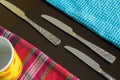 Three silver knives between blue and multicolor napkins with yellow cup on the dark reflective backdrop. Royalty Free Stock Photo