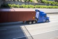 Blue comfort long haul big rig semi truck with long container driving on the divided highway road running under bridge Royalty Free Stock Photo