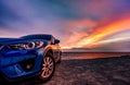 Blue compact SUV car with sport and modern design parked by beach at sunset. Hybrid and electric car technology. Car parking space