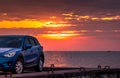 Blue compact SUV car with sport and modern design parked on concrete road by sea at sunset. Environmentally friendly technology. Royalty Free Stock Photo