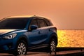 Blue compact SUV car with sport and modern design parked on concrete road by sea at sunset. Environmentally friendly technology. Royalty Free Stock Photo