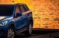 Blue compact SUV car with sport and modern design parked on concrete road by sea at sunset. Environmentally friendly technology. Royalty Free Stock Photo