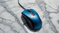 A blue computer mouse with a black cable on a marble patterned surface Royalty Free Stock Photo