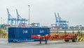 Blue container, red semitrailer and cranes in a port terminal