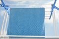 A blue cotton face towel on a plastic multi layers clothes hanger drying rack against the blue cloudy sky, laundry, homework