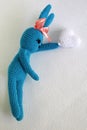 A blue crocheted banny rabbit takes a white heart and lies on a white background