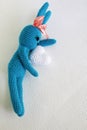 A blue crocheted banny rabbit takes a white heart and lies on a white background