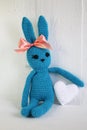 A blue crocheted banny rabbit takes a white heart and sits on a white background