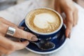 Blue cup with cappuccino with heart-shaped foam in female hands at a table in a cafe. Close-up. Soft focus