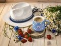 A blue cup of coffee with daisies, a bouquet of daisies and cornflowers, strawberries, a hat from the sun. Royalty Free Stock Photo