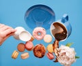 Blue cup with coffee, donuts, macaroons, peony and hand holding milk cream jug flying over a blue background Royalty Free Stock Photo