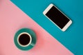 A blue cup with coffee and a mobile phone stands on a pink and blue background. Morning breakfast, business