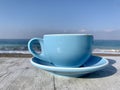 blue cup of coffee on wooden table in bar on sand beach over blue sky and sea on day noon light background. Royalty Free Stock Photo