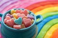 A blue cup filled with candy hearts sits atop a vibrant rainbow colored table, A pot full of heart-shaped candies on a rainbow, AI Royalty Free Stock Photo