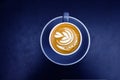 Blue cup of fresh cappuccino with latte art on dark metal table background