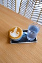 Blue cup of tasty cappuccino with beautiful latte art and glass of water