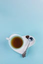 Blue cup of tea with silver spoon and one chocolate candy on white saucer in heart shape on light blue background. Royalty Free Stock Photo