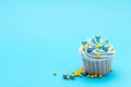 Blue cupcake decorated with candy balls on bright blue background