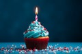 Blue cupcake, red sprinkles, and a lit candle on blue backdrop