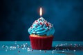 Blue cupcake, red sprinkles, and a lit candle on blue backdrop