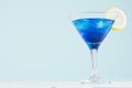 Blue curacao cocktail with ice cubes, lemon slice in luxury martini glass on white wood board and pastel mint color wall. Royalty Free Stock Photo