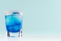 Blue curacao cocktail with ice cubes and sugar rim in shot glass on elegant white wood board and pastel mint color wall. Royalty Free Stock Photo